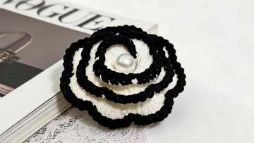 Luxury black and white crocheted camellia flower with pearl center on a fashion magazine, representing 2026 floral crochet design trends.